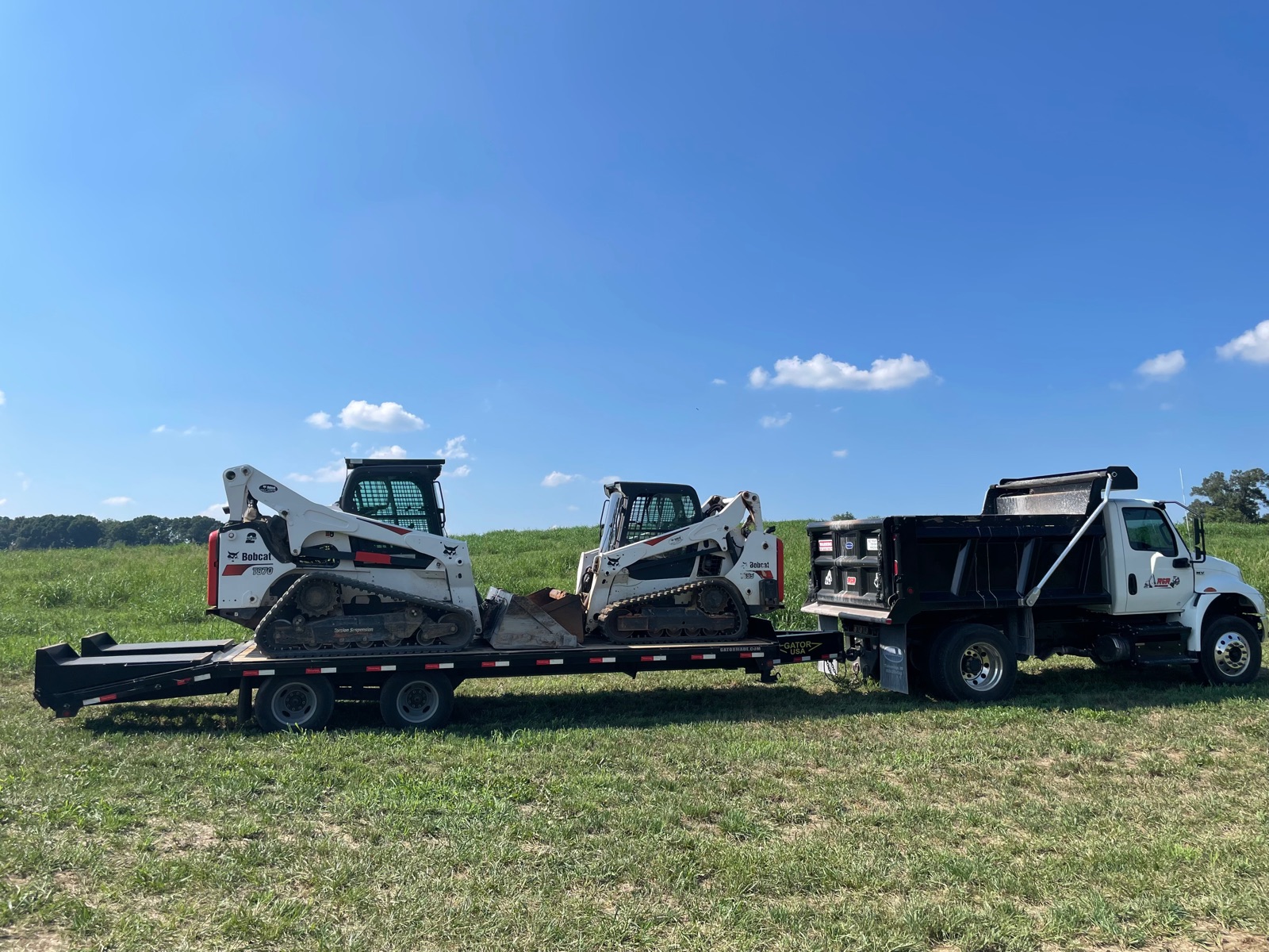 Two skid steers and a dump truck loaded on a flatbed trailer