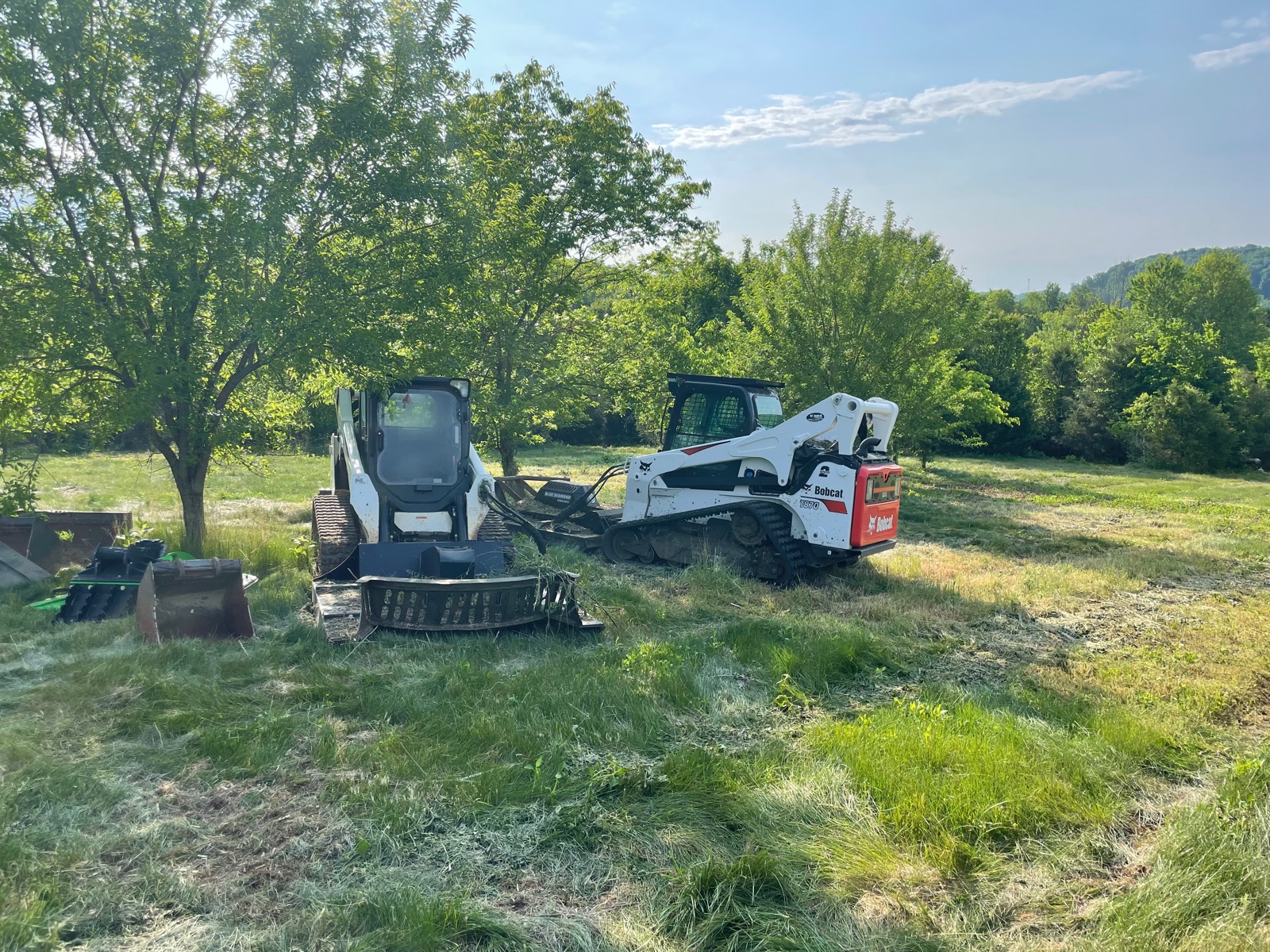 Two skid steers with brush mower attachments parked in a freshly cut field