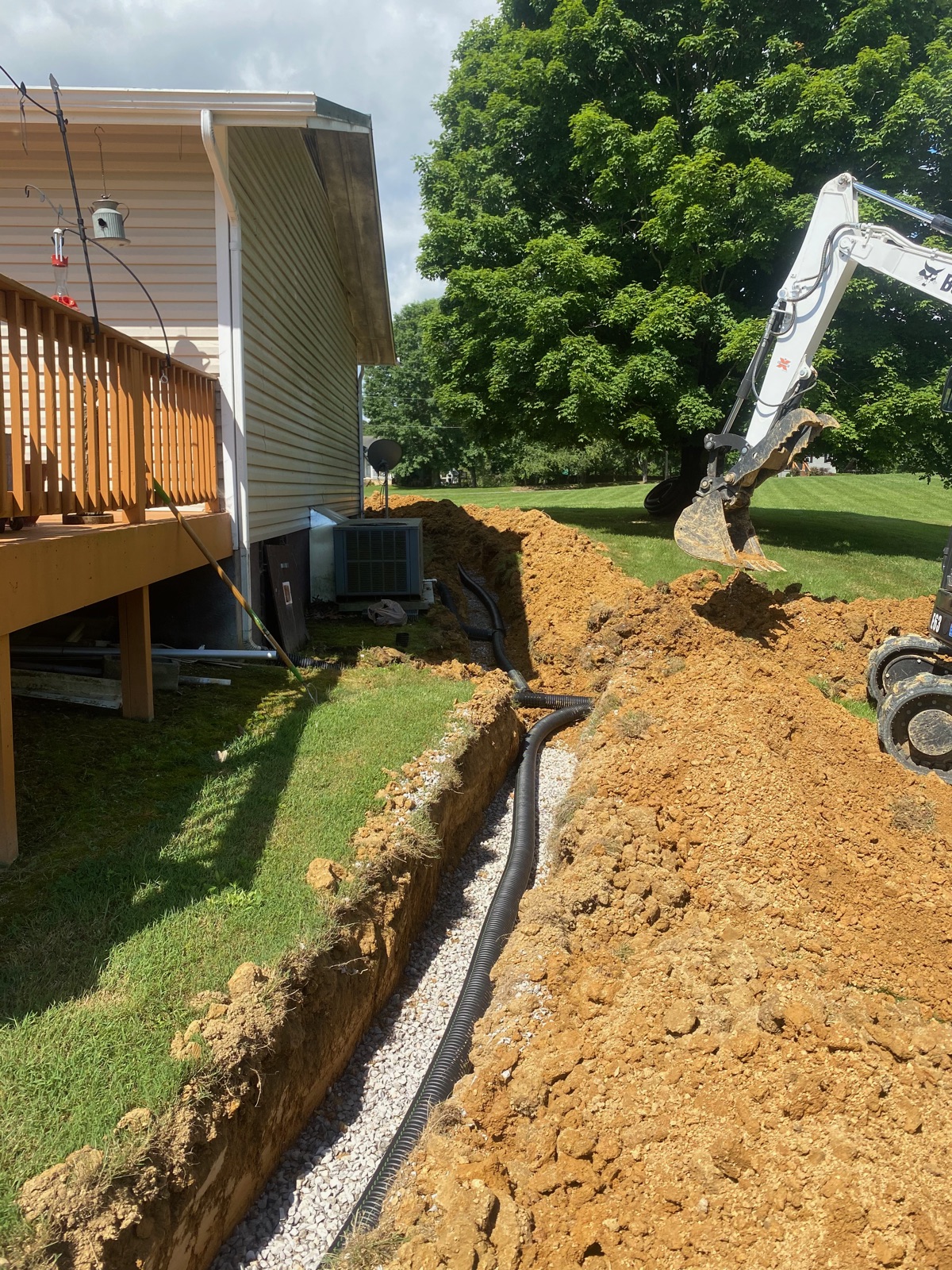 Excavator working a drainage trench beside a home