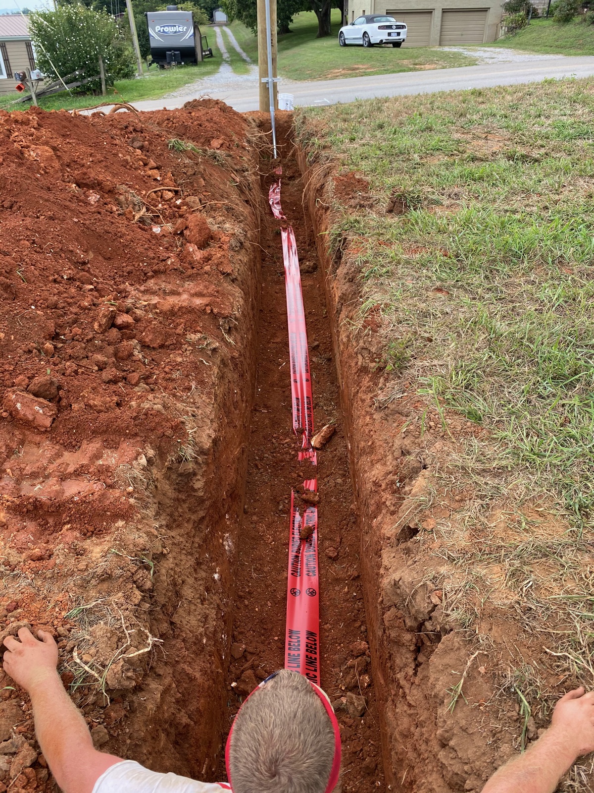 Deep utility trench with red conduit running toward a residence