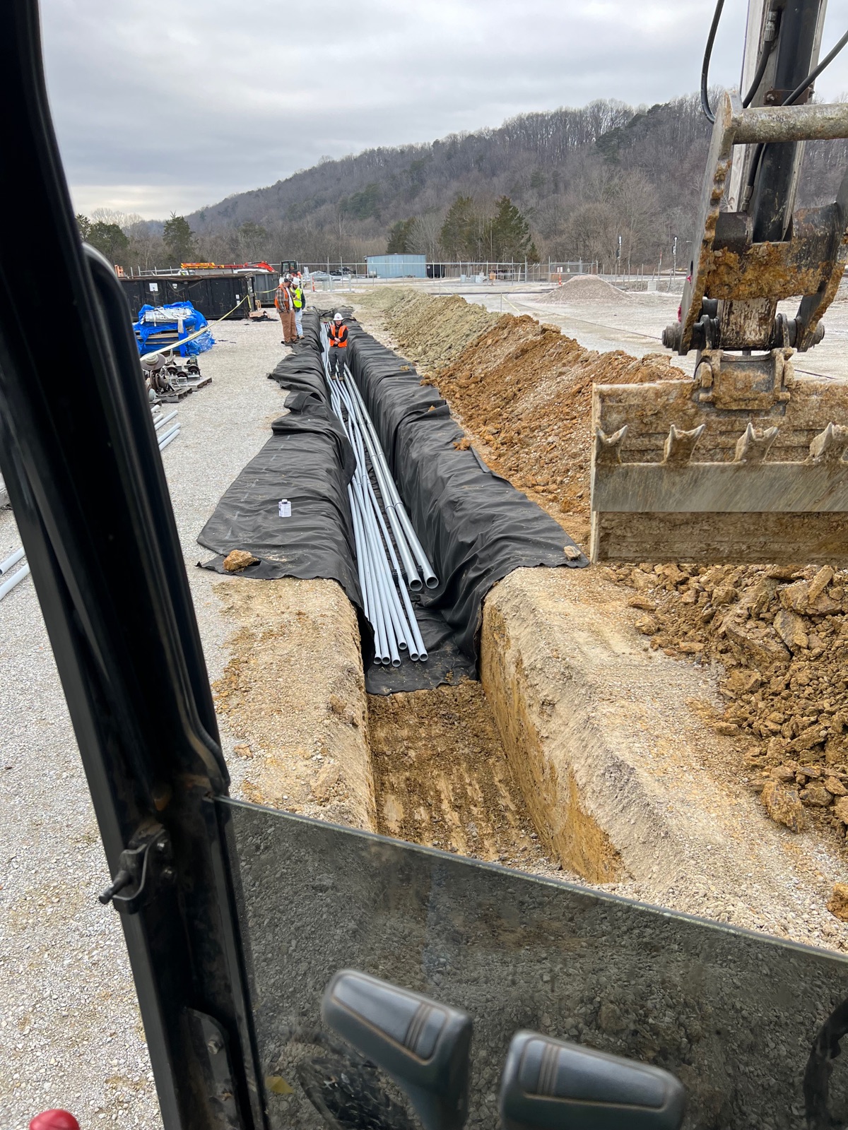 Excavator and crew laying PVC utility lines in a long commercial trench