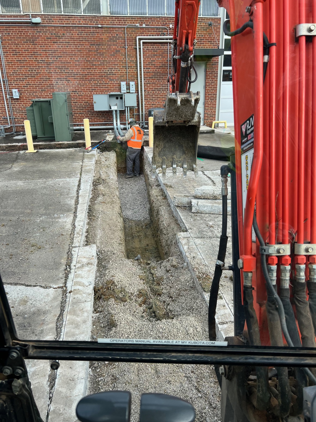 Trench cut next to a brick commercial building with excavator working overhead