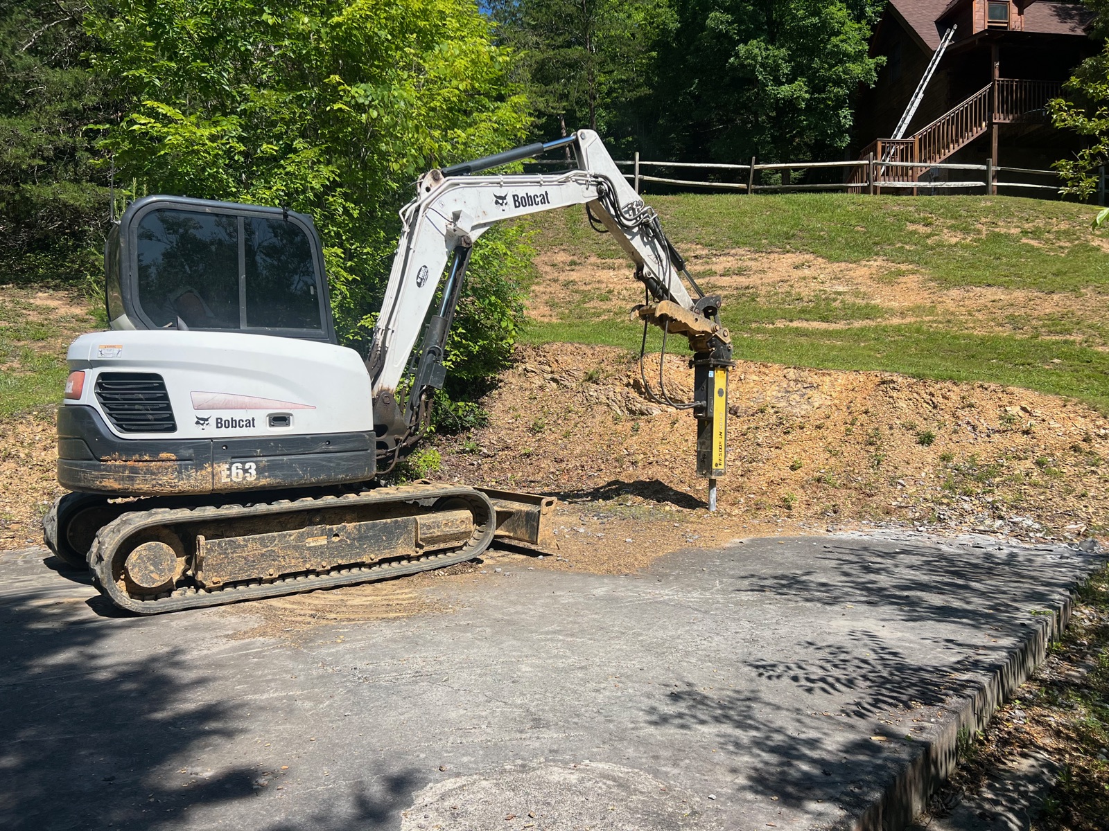 Bobcat excavator with hydraulic hammer attachment on a driveway