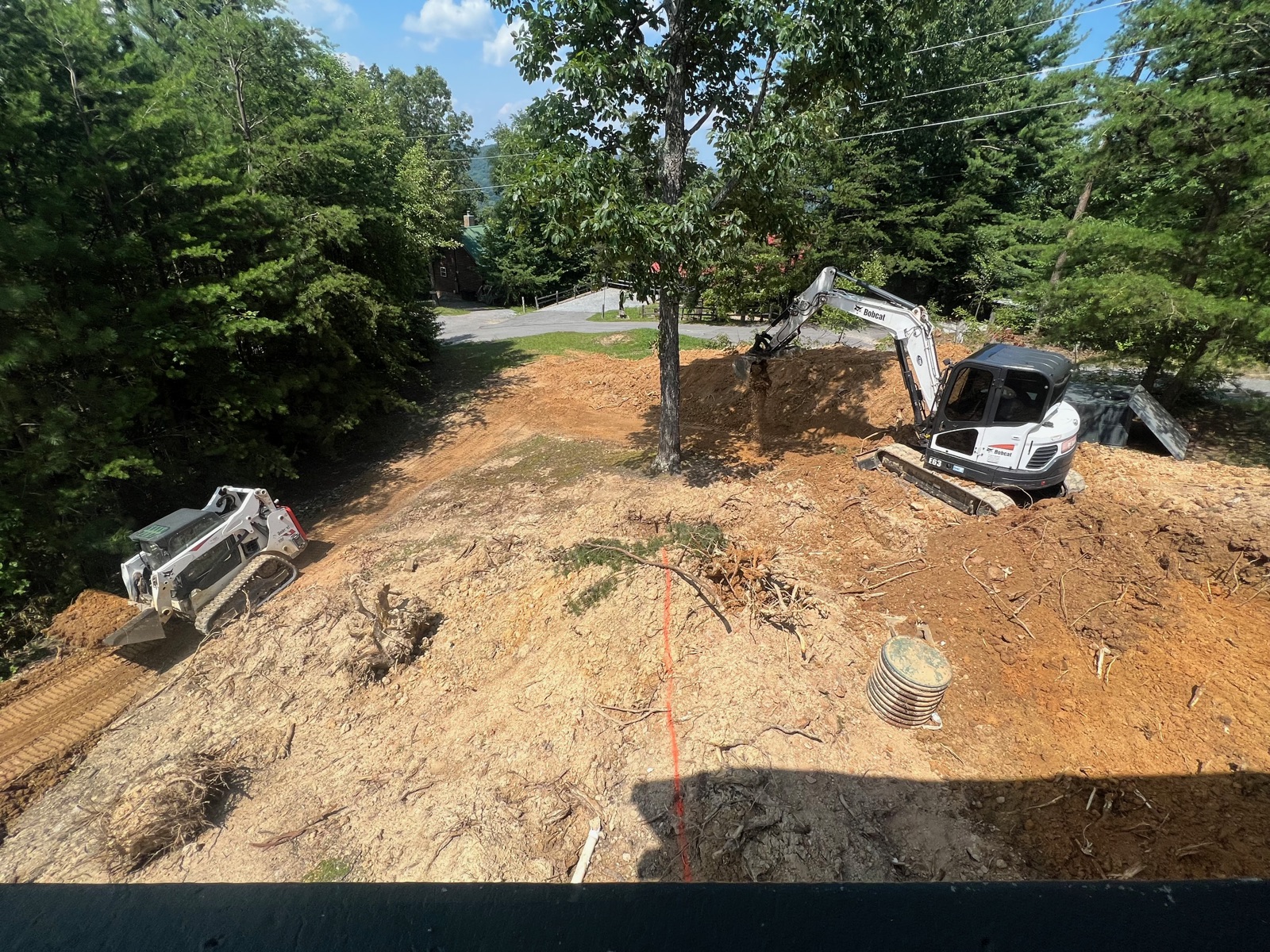 Excavator and skid steer working a wooded residential lot from above
