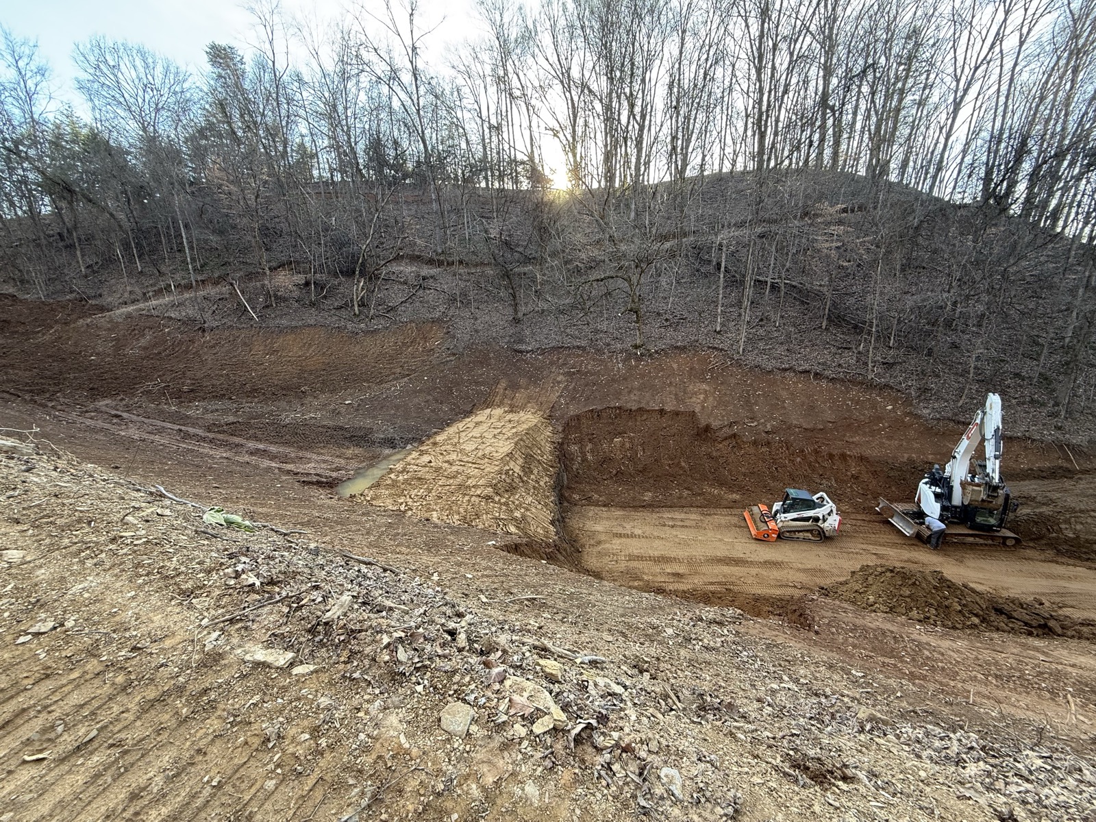 Excavator and skid steer working a steep dirt cut