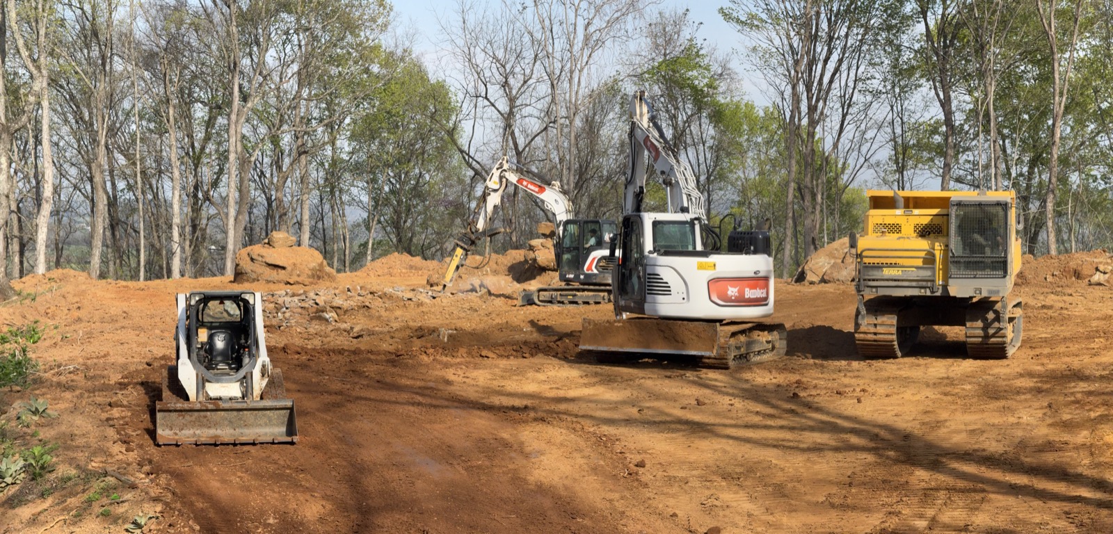 Skid steer, excavator, and dump truck on a cleared site
