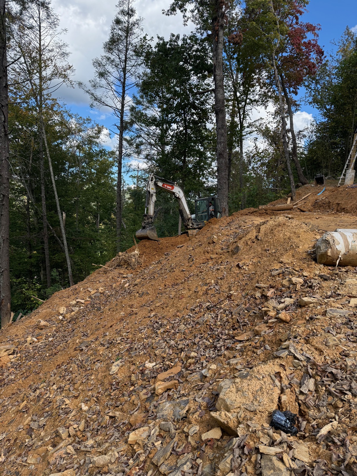 Excavator carving a new driveway out of a rocky wooded slope